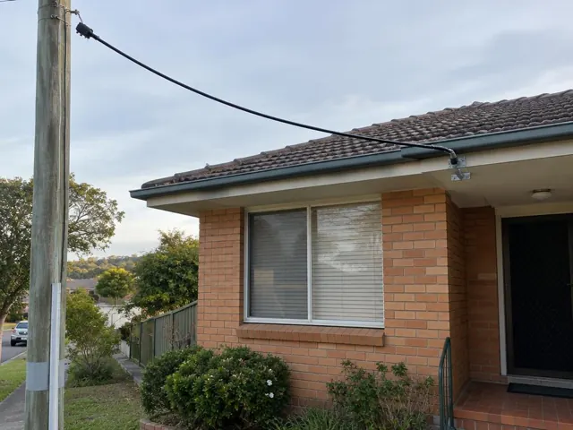 Overhead service cable and point-of-attachment bracket on a brick house exterior in Brookvale